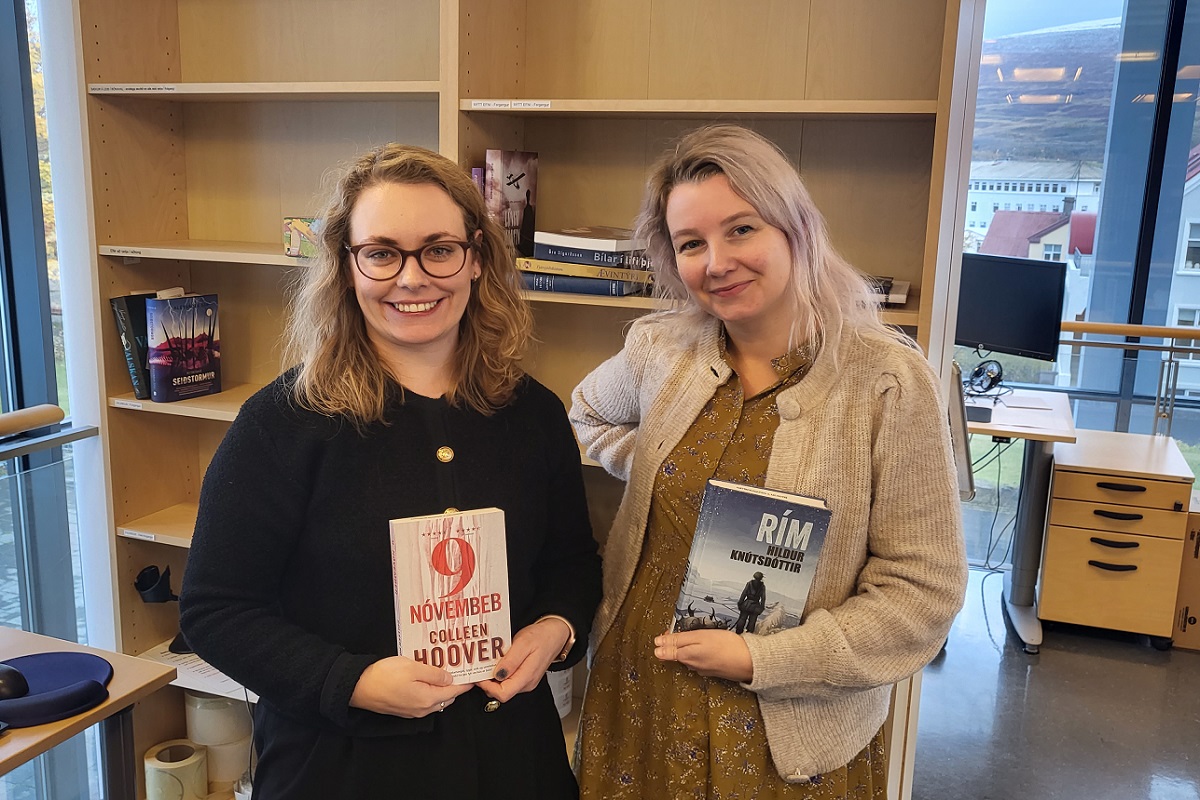 Two women in front of bookshelves, each holding a book
