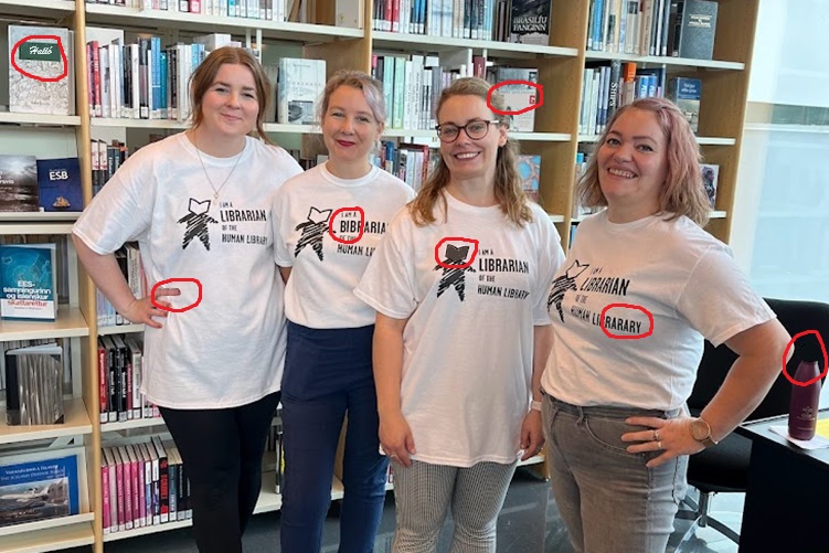 Four women standing in front of bookshelves wearing t-shirts marked Human Library